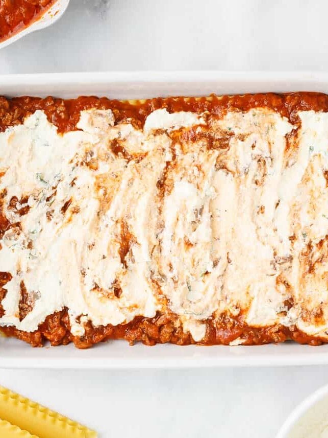 Ricotta filling over meat sauce in a baking dish.