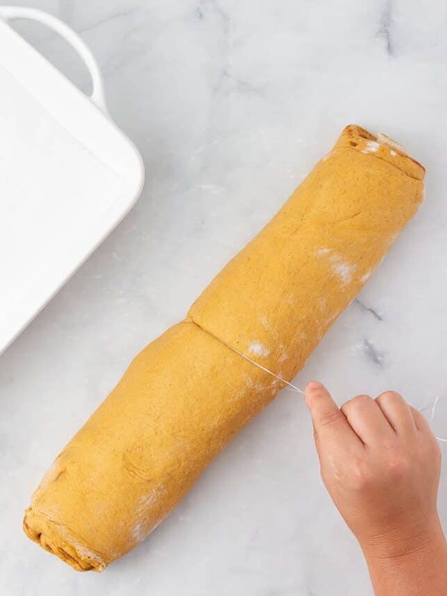 Slicing pumpkin cinnamon roll dough into pieces.