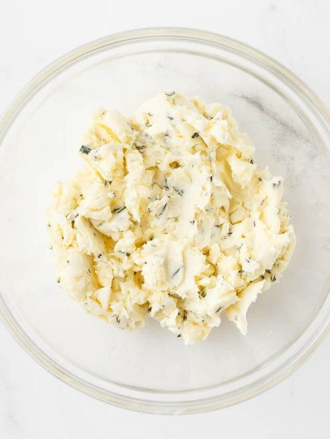 Butter with garlic and rosemary in a glass bowl.