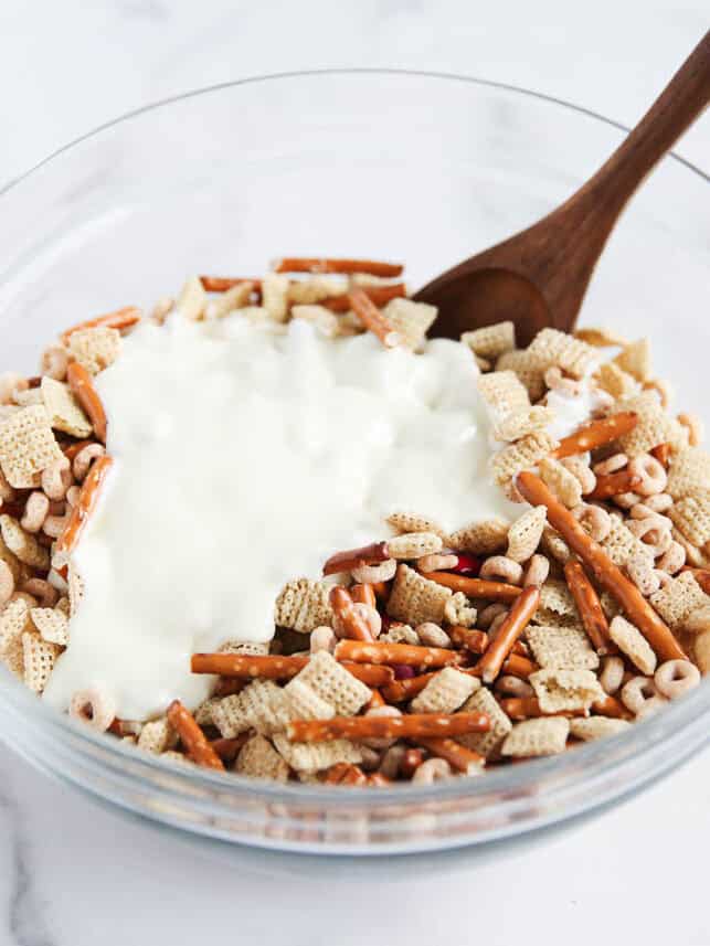 Pouring white chocolate over Christmas chex mix.