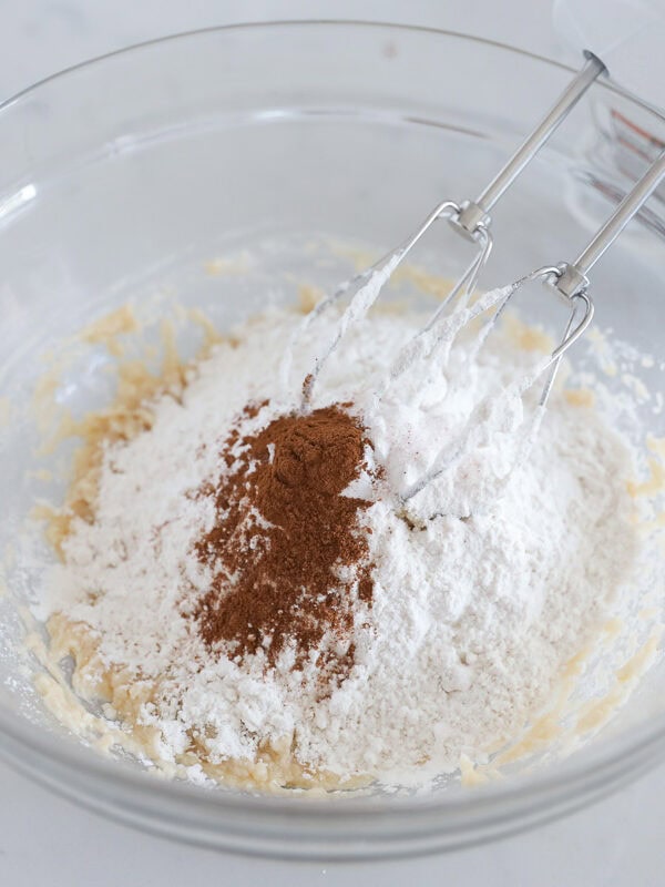 Butter, sugar, eggs, vanilla and dry baking staples in a bowl with beaters from a mixer.