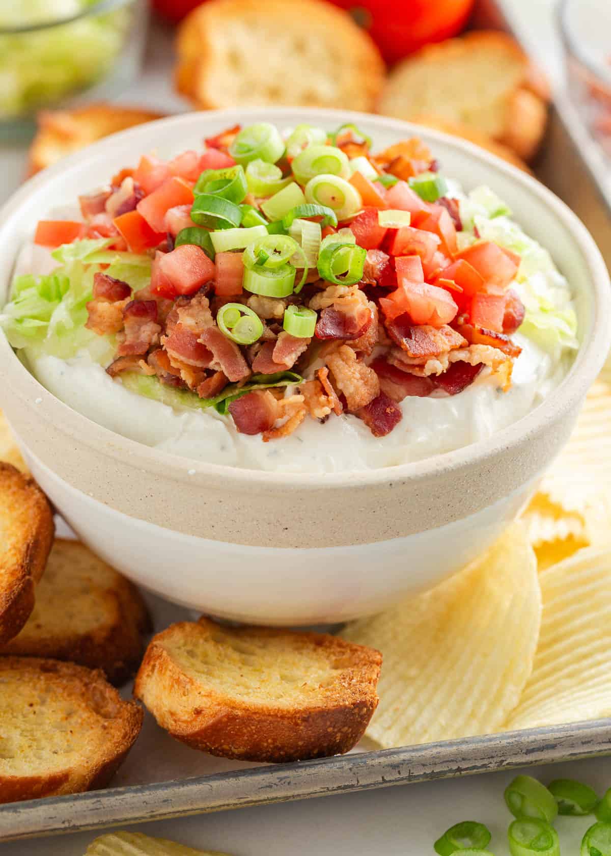 BLT dip in a bowl with crostini and chips on a platter.