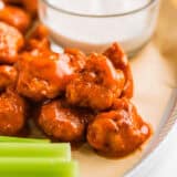 Boneless chicken wings on a serving plate with dip and celery.