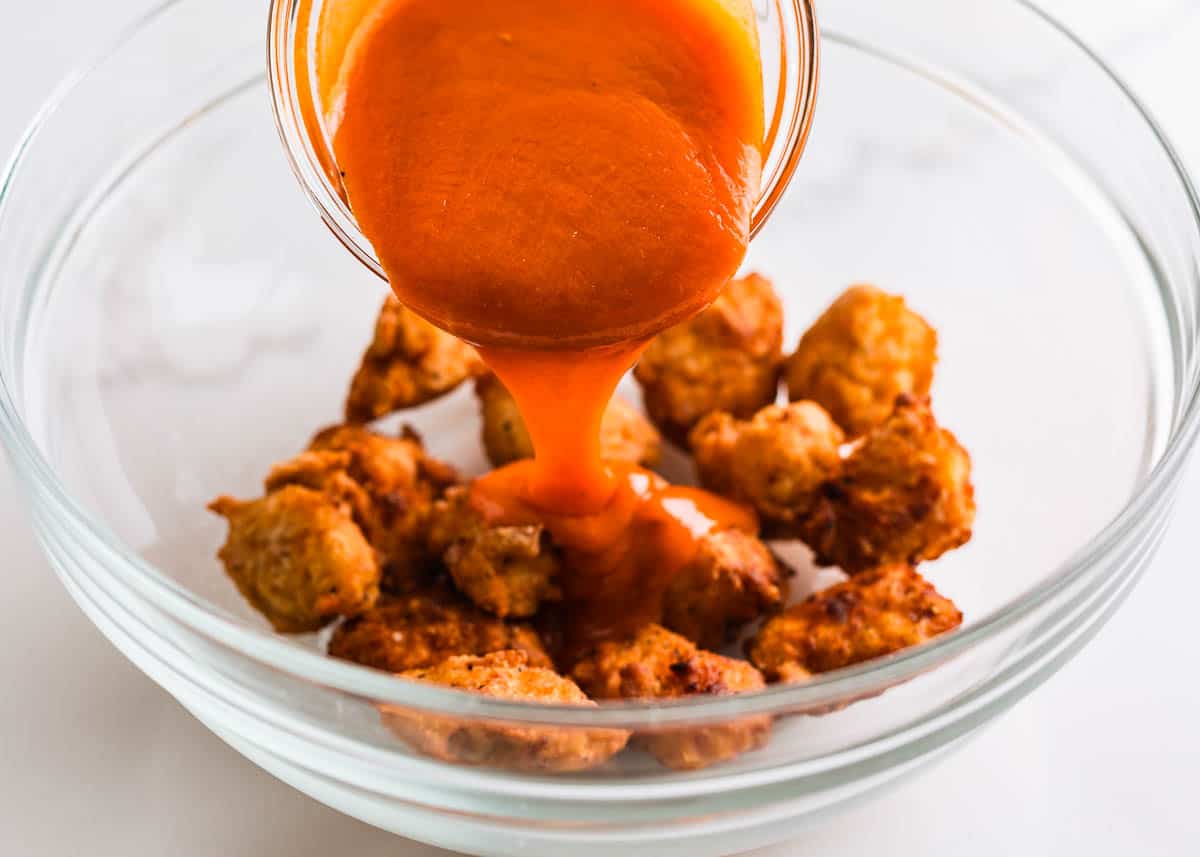 Pouring buffalo sauce over boneless chicken wings. 