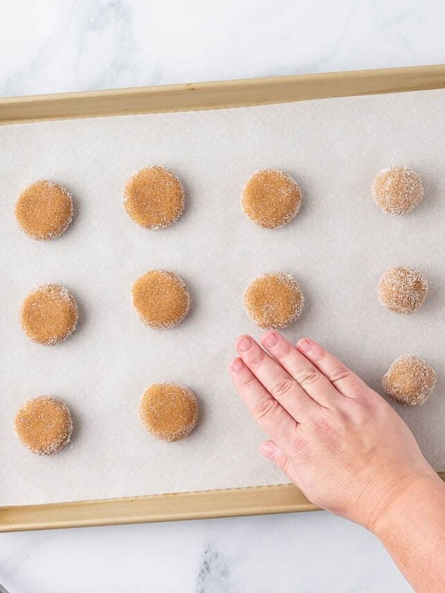 Showing dough balls rolled in sugar on a baking sheet then pressed flat.