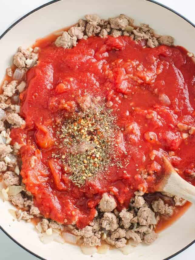 Ground beef with tomato sauce and seasonings in a skillet.