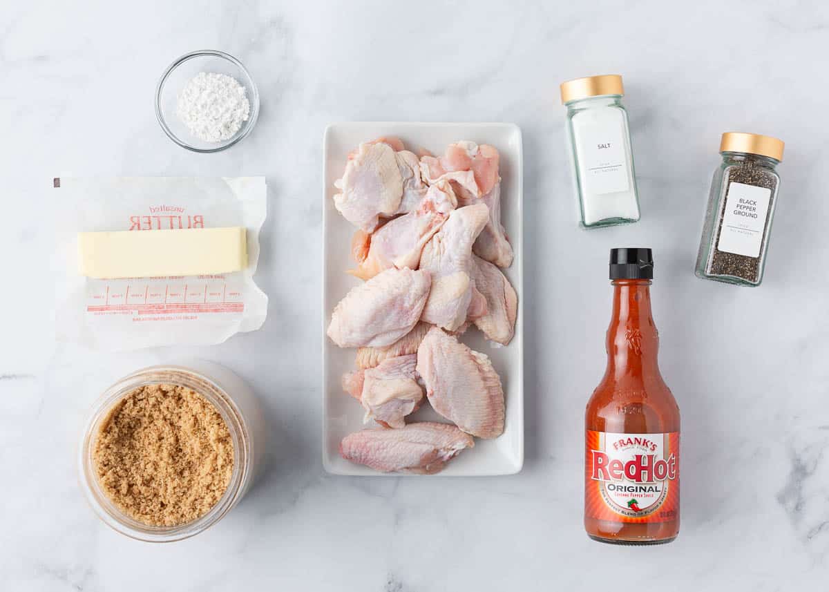 Chicken wings, hot sauce, butter and baking powder on the counter. 