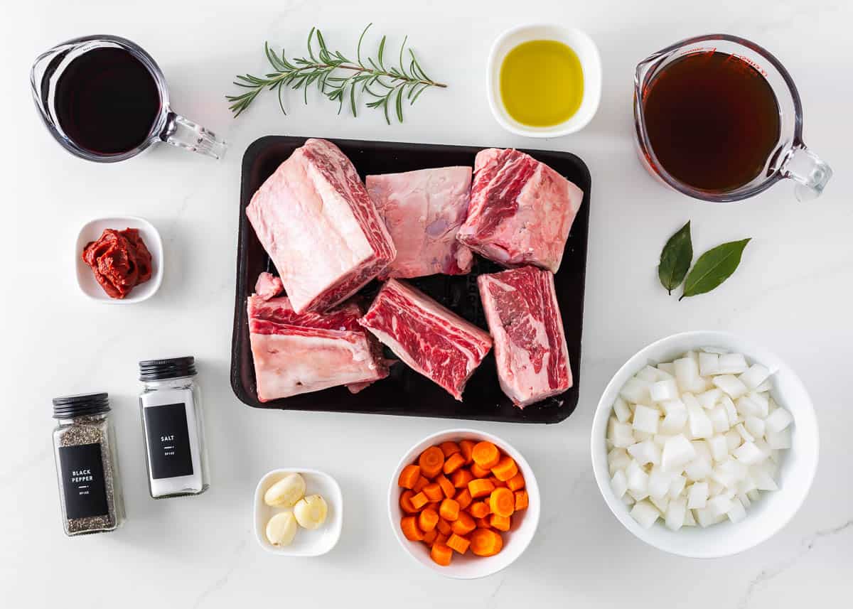 Beef short ribs, onion, carrots, red wine, beef stock, thyme, bay leaves and garlic on the counter.