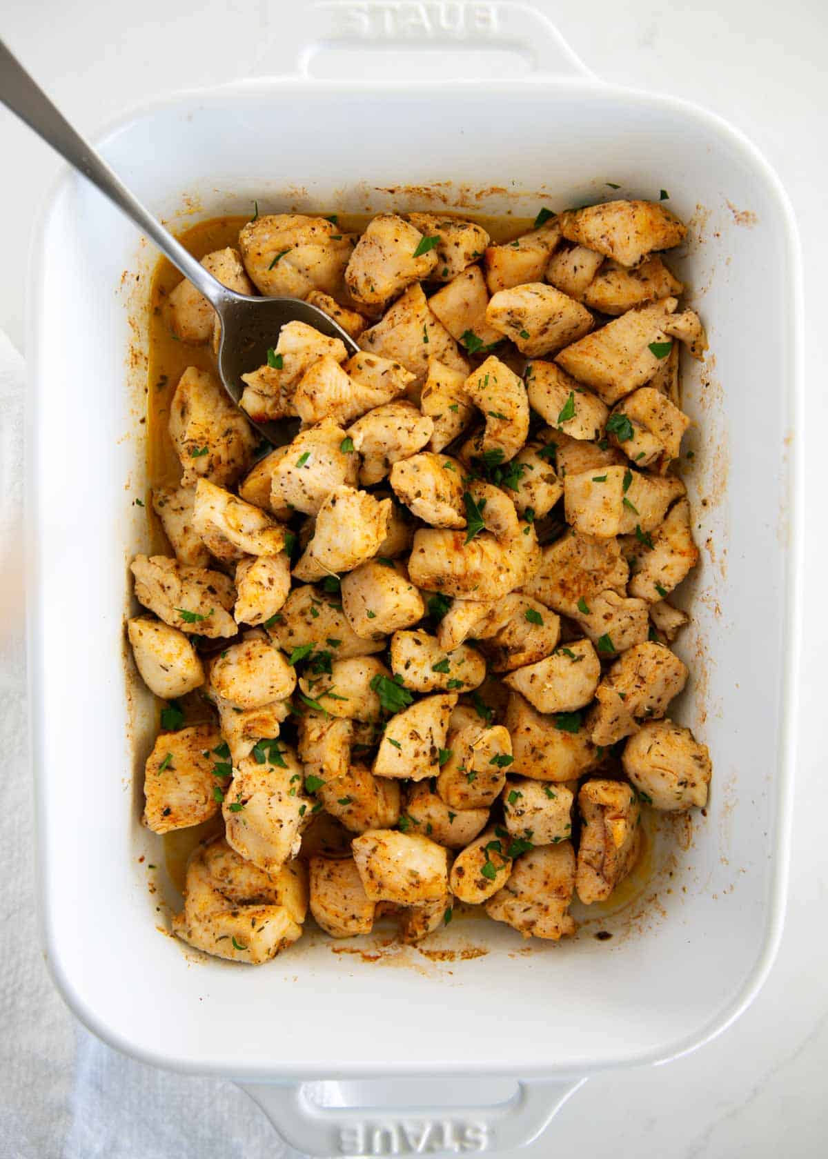 Oven baked chicken bites in white baking dish.