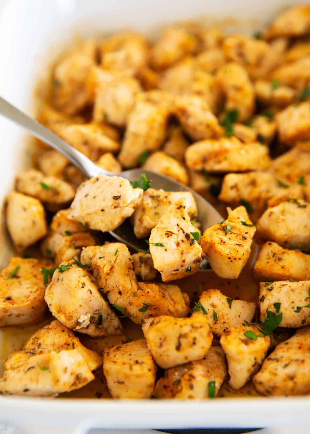 Baked chicken bites in baking dish with serving spoon.