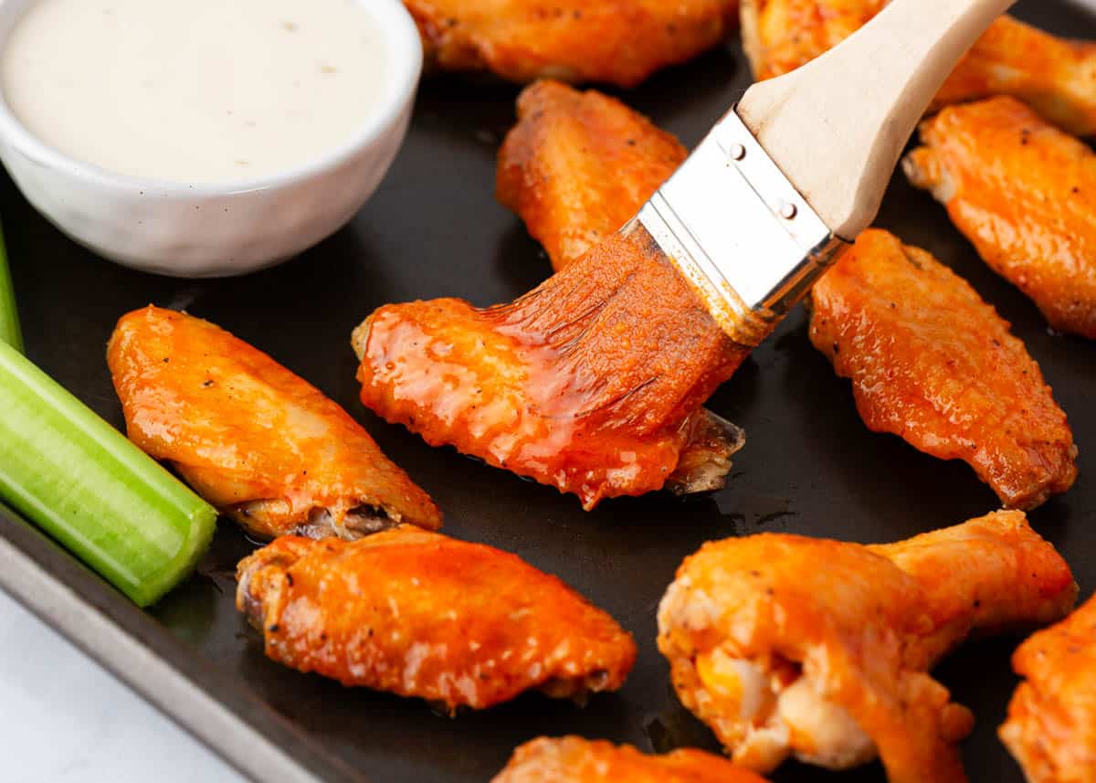 Brushing oven baked chicken wings with buffalo sauce.