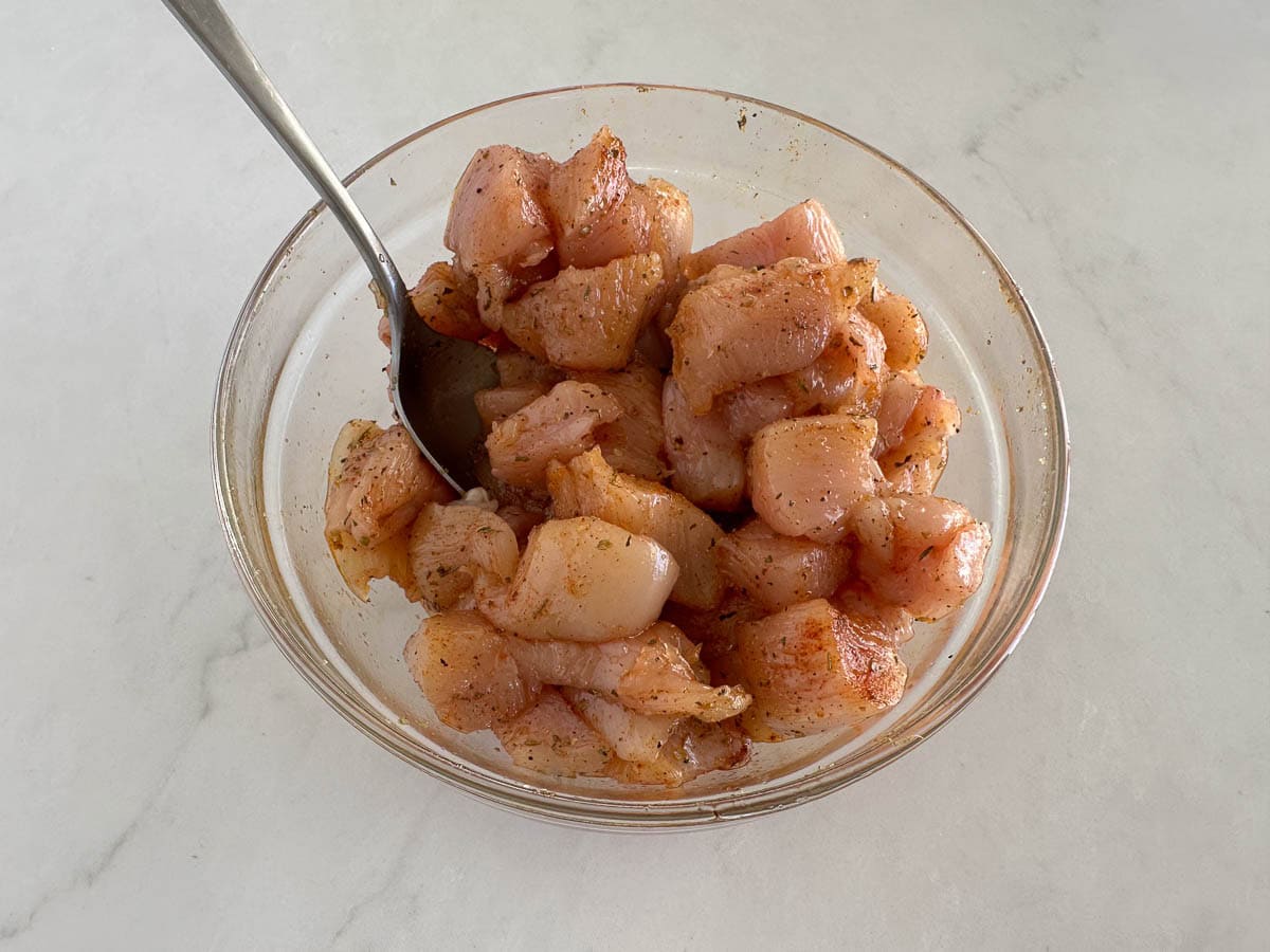 Stirring chicken bites in a bowl with seasonings