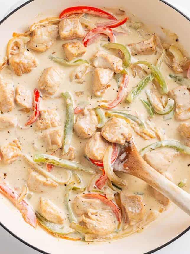 Chicken, peppers and onion in a creamy sauce in a skillet.