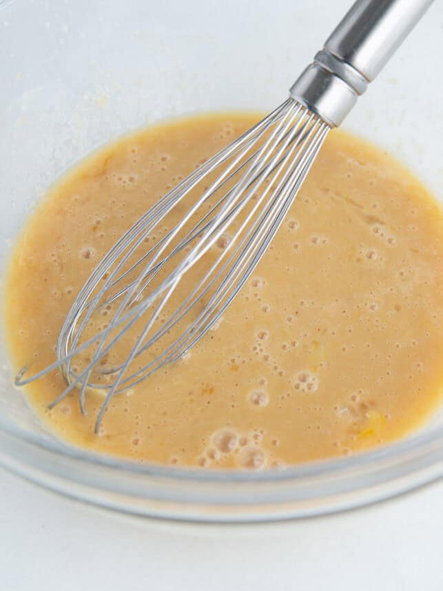 Whisking eggs, milk, applesauce and vanilla extract in a bowl with whisk.