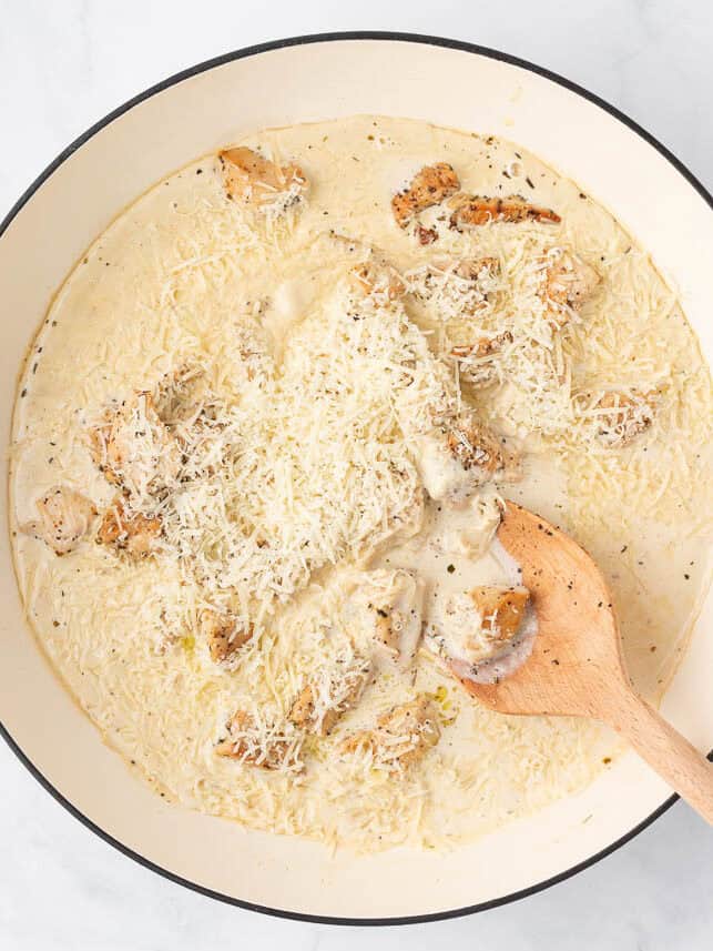 Creamy sauce with chicken and parmesan in a skillet.