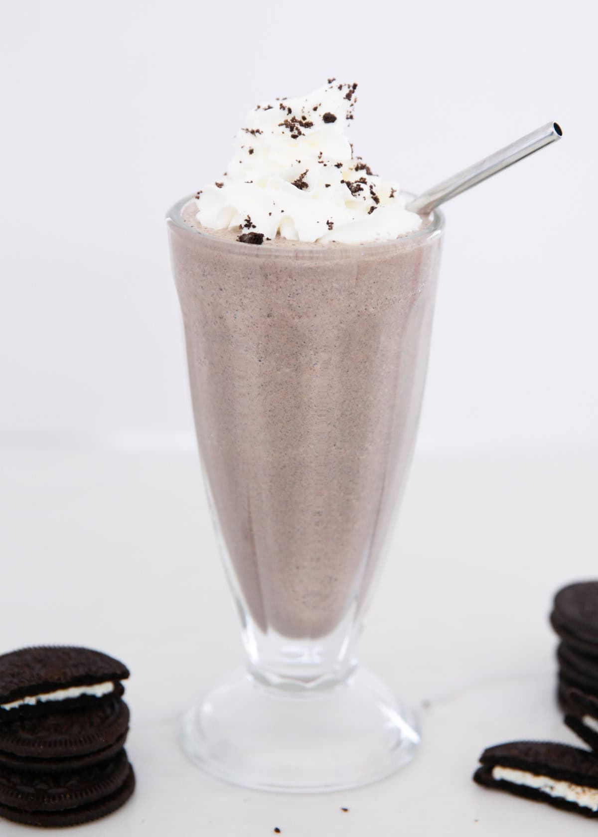 Oreo milkshake in a glass cup with metal straw.